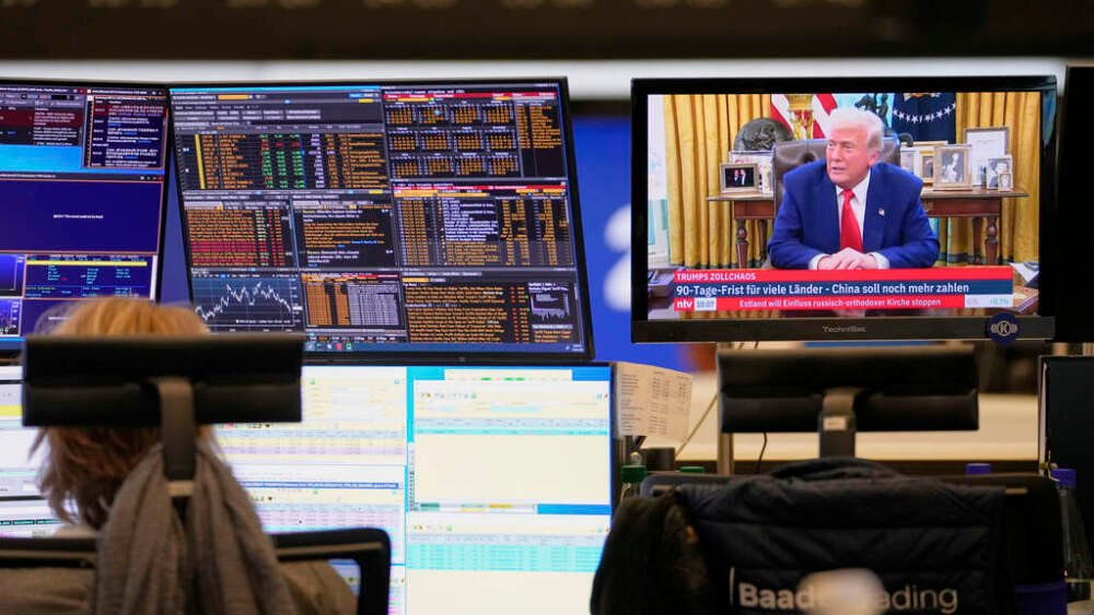 A trader sits in front of computer screens on the trading floor of the Frankfurt Stock Exchange beside a TV showing U.S. President Donald Trump on a news channel in Frankfurt, Germany, the day after Trump's announced a 90-day pause on 'reciprocal' tariffs, Thursday, April 10, 2025. (AP Photo/Martin Meissner)